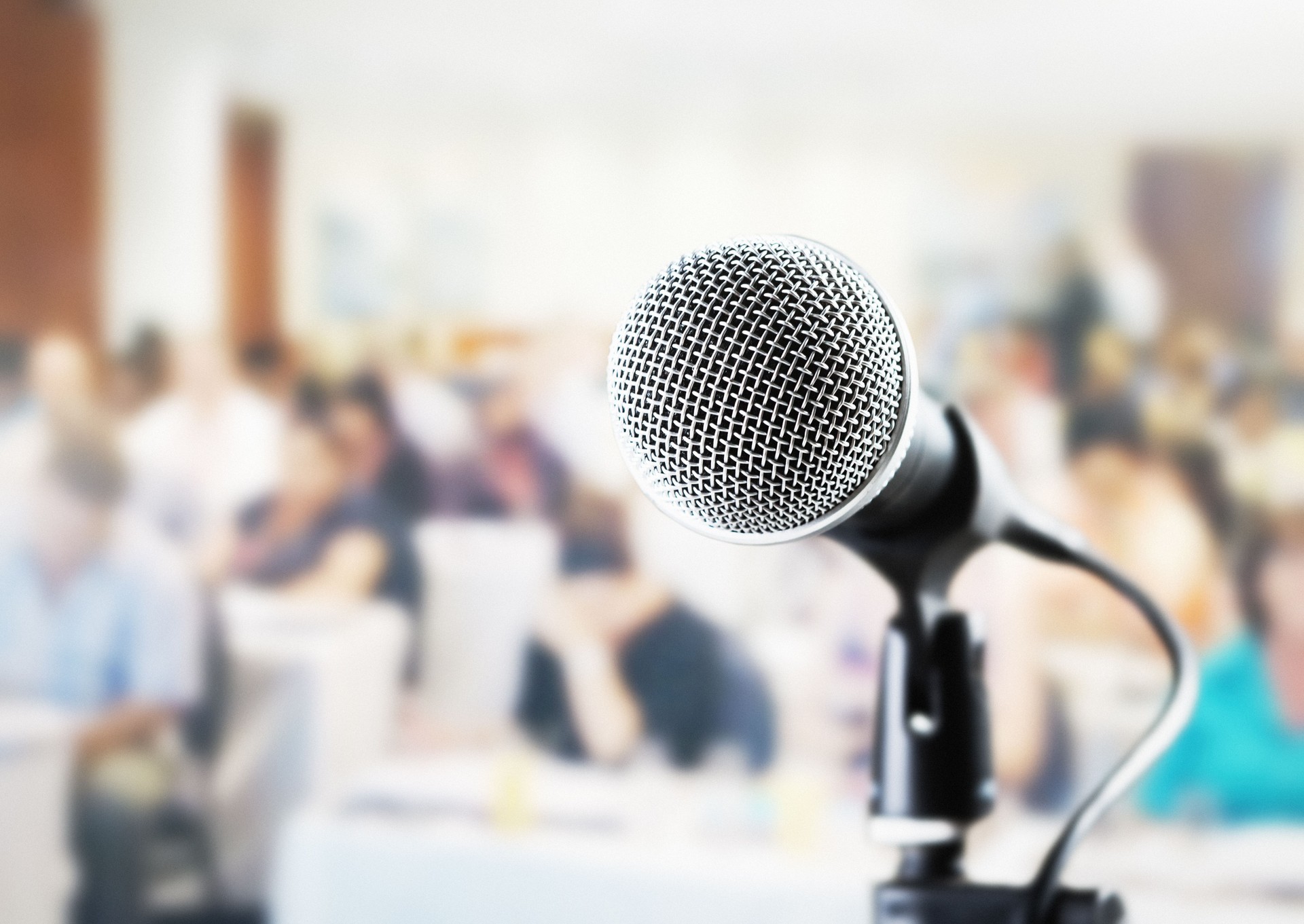Vocal microphone awaiting public speaker at a seminar or conference, with blurred attendees sitting at tables